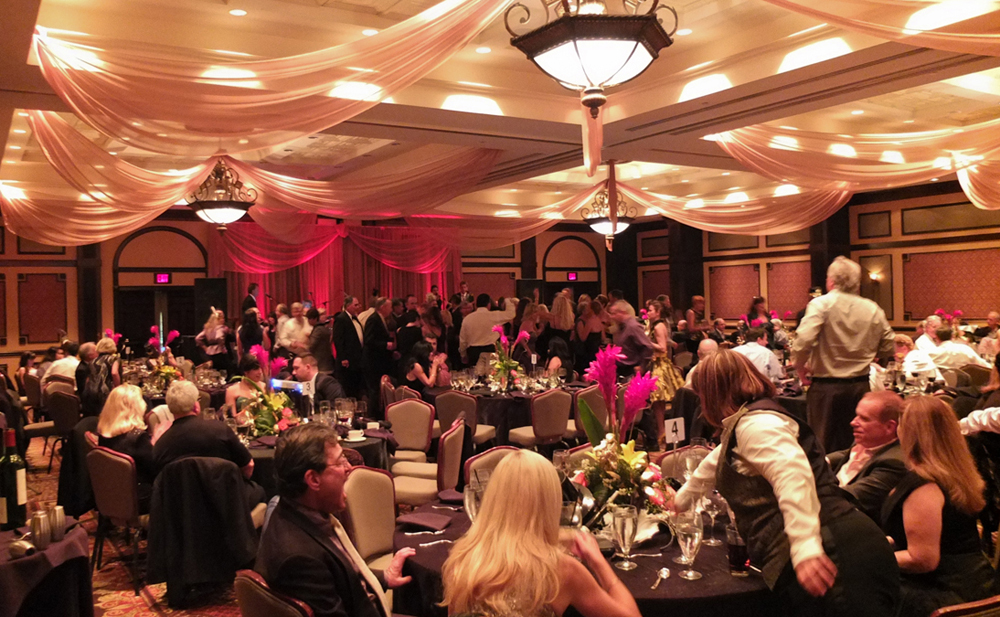 Custom event ceiling draping and backdrop in gold chiffon with red LED up-lights for a New Year's Eve party at Hammock Beach Resort in Palm Coast, FL. Photo and drapes by W Drapings.
