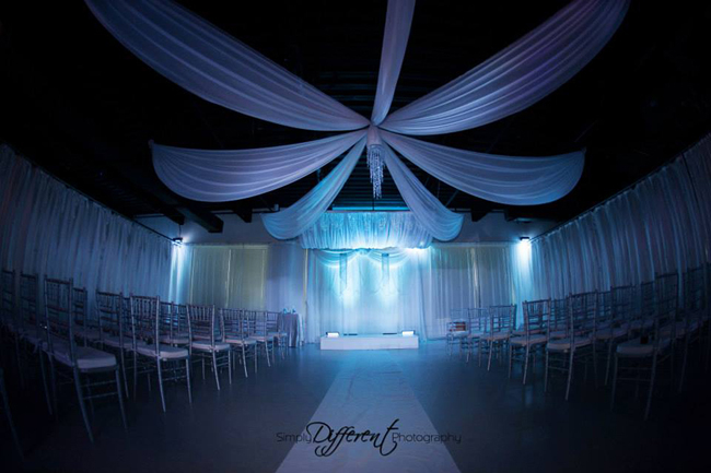 Custom ceiling draping, backdrop, and canopy in white chiffon with decorative strings of crystal beads, chandeliers and LED up-lights for a modern wedding reception at Heaven Event Center in Orlando, FL. Draping and accessories by W Drapings. Photo by Simply Different Photography.