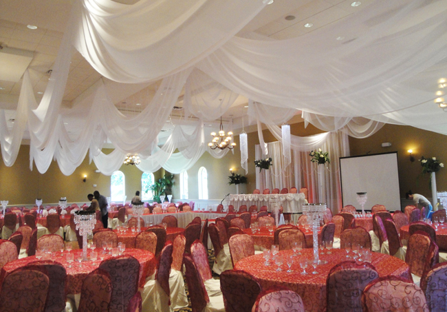 Classic wedding reception at Holy Trinity Reception Center in Maitland, FL with custom event draping and backdrop in white chiffon by W Drapings. Accessories include decorative crystal chandeliers. Photo and drapes by W Drapings.
