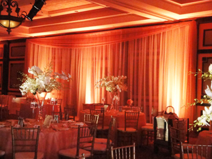 Custom backdrop in ivory chiffon with amber LED up-lights for a traditional wedding reception at Hammock Beach Resort in Palm Coast, FL. Photo and drapes by W Drapings.